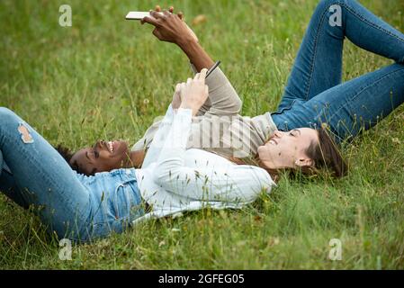 Giovani amici femmine sdraiati sull'erba mentre usano lo smartphone nel parco Foto Stock