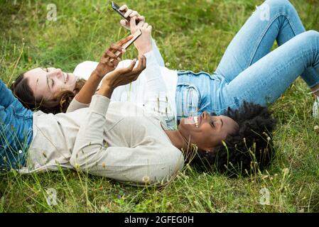 Giovani amici femmine sdraiati sull'erba mentre usano lo smartphone nel parco Foto Stock