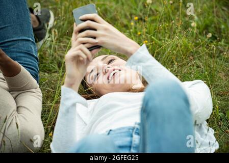 Giovani amici femmine sdraiati sull'erba mentre usano lo smartphone nel parco Foto Stock