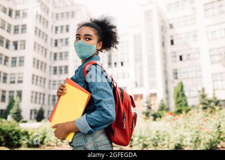 Studentessa nera che posa in maschera medica faccia in piedi all'esterno Foto Stock