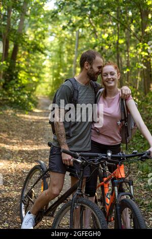 Sorridente giovane coppia in piedi con biciclette nella foresta Foto Stock