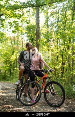 Il giovane uomo bacia sulla testa della donna mentre si trova in piedi con le biciclette nella foresta Foto Stock