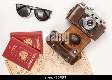 Mappa del mondo, due passaporti, una vecchia macchina fotografica in una custodia di pelle e occhiali da sole su un tavolo di legno bianco. Vista da above.inscription - passaporto russo Foto Stock