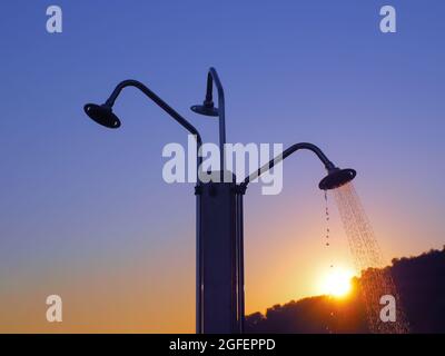 Doccia tripla sulla spiaggia con un ruscello da una delle lattine d'acqua sullo sfondo del sole Foto Stock