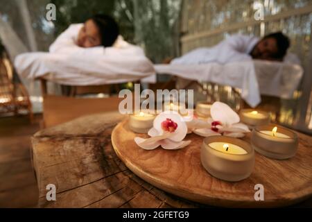 Massaggio aromatico per coppia. Coppia sdraiata su tavoli da massaggio durante il giorno-spa e romantico week-end con candele e fiori di orchidea presso il centro termale Foto Stock