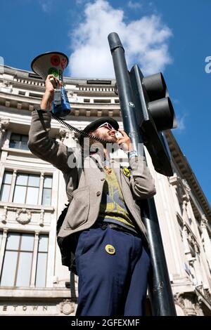 Londra, Regno Unito. 25 Agosto 2021. Un manifestante canta in un megafono mentre i manifestanti della ribellione di estinzione scendono su Oxford Circus, dove hanno bloccato il traffico con un gigantesco tavolo rosa, ballato pacificamente e sentito discorsi, mentre le manifestazioni climatiche a Londra continuano il 25 agosto 2021. Credit: Kieran Riley/Pathos Credit: One Up Top Editorial Images/Alamy Live News Foto Stock