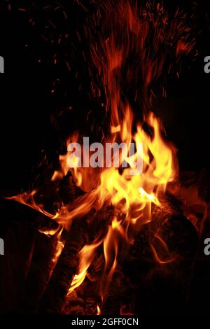 Un fuoco che brucia, tronchi di legno, scintille rosse e fiamme gialle su sfondo scuro Foto Stock