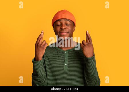 Fare il desiderio. Ritratto del giovane Guy nero tenendo le dita incrociate Foto Stock