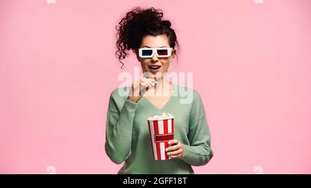 donna sorpresa in 3d occhiali che tengono popcorn isolato sul rosa Foto Stock