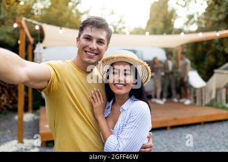 Giovane coppia felice diverse prendere selfie al campo, riposare con gli amici vicino rimorchio, trascorrere il fine settimana autunno all'aperto Foto Stock