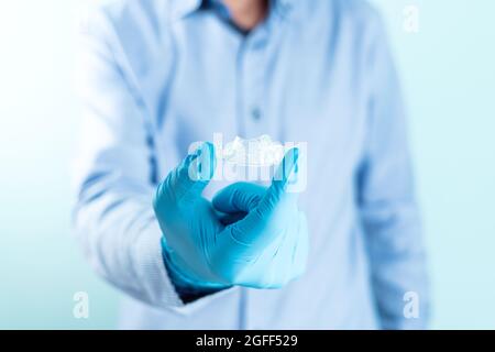 Medico in camicia blu e guanti che mostrano una spinza dentale trasparente. Foto Stock