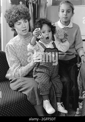 Austin Texas USA, circa 1988: La donna tiene il suo bambino adottò Honduran sul suo grembo con il suo bambino naturale guarda sopra. ©Bob Daemmrich Foto Stock