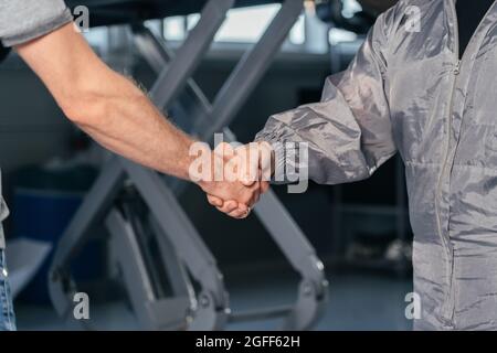 Il meccanico agita le mani con il proprietario dell'auto nel garage dell'officina. Concetto di servizi auto Foto Stock