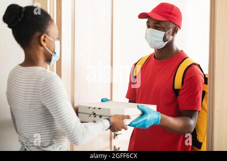 Black Woman che riceve l'ordine prendendo scatole pizza dal deliveryman Indoor Foto Stock