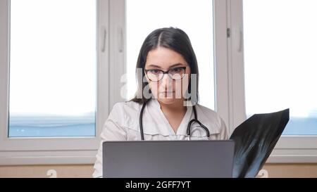 Medico con occhiali controlla l'immagine radiografica dei piedi in ufficio Foto Stock