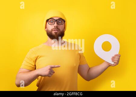 uomo che tiene il marcatore di posizione e che lo punta su sfondo giallo, navigazione concettuale ed esplorazione Foto Stock