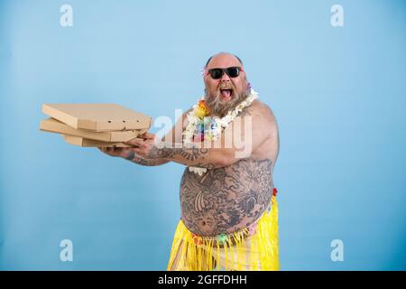 Felice uomo obeso in erba gonna e fiori garland tiene pizze su sfondo azzurro chiaro Foto Stock