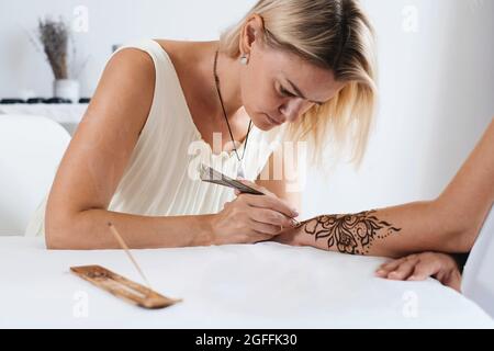 Artista che applica il tatuaggio henné sulle mani delle donne. Il Mehndi è un'arte decorativa indiana tradizionale, a mano con mehendi floreali. Disegno di bellezza per matrimoni e. Foto Stock