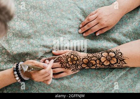 Artista che applica il tatuaggio henné sulle mani delle donne. Il Mehndi è un'arte decorativa indiana tradizionale, a mano con mehendi floreali. Disegno di bellezza per matrimoni e. Foto Stock