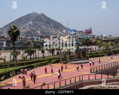 Muninet Parque la Muralla, Lima - Sep 2019: Gruppo di bambini nel campo sportivo in uniformi rosse. Sullo sfondo le baraccopoli sul lato di Cerro SA Foto Stock