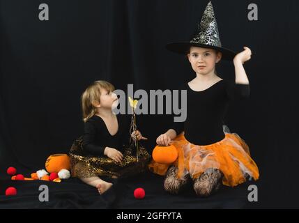 Due sorelle vestite come streghe per la festa di Halloween in abiti neri, un cappello con una ragnatela, una gonna arancione e un secchio di zucca per dolci Foto Stock