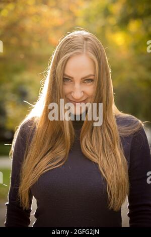 Bella giovane donna su uno sfondo di alberi autunnali. Concetto di emozione. Passeggiata nel parco autunnale. Riprese retroilluminate. Foto Stock