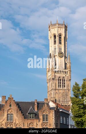 Brugge, Fiandre, Belgio - 4 agosto 2021: Torri campanarie illuminate da sole su facciate di mattoni marroni di piazza Burg sotto il paesaggio blu nuvoloso. Alcune foglie verdi Foto Stock