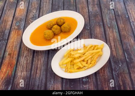 Porzione di polpetta di manzo in salsa servita su un vassoio bianco e guarnita con patate tagliate a mano fritte in olio d'oliva. Foto Stock