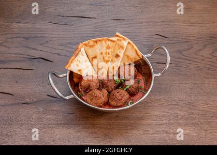 Casseruola di metallo con polpette di manzo in salsa di pomodoro con prezzemolo e verdure stufate e pezzetti di pita di pane da bagnare Foto Stock