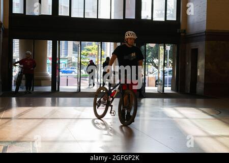 Wellington Nuova Zelanda - Luglio 31 2021; il ciclista spinge il ciclo attraverso le lunghe ombre interne della stazione ferroviaria con le persone che si muovono attraverso. Foto Stock