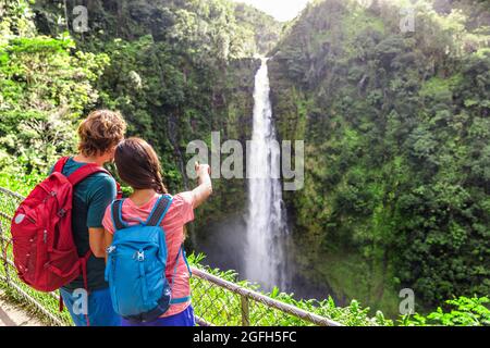 Coppia di turisti sulle Hawaii a cascata. Ragazza turistica che punta alla cascata di Akaka Falls sulle Hawaii, Big Island, USA. Turismo Viaggi concetto giovani Foto Stock