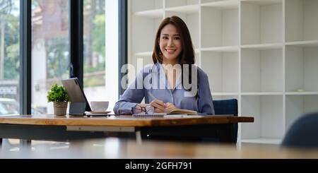 Foto di una splendida segretaria che lavora in ufficio, seduta alla scrivania di legno Foto Stock
