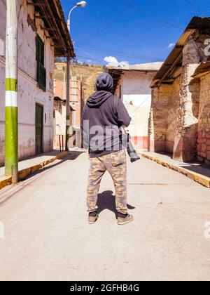 Escursionista fotografo con la fotocamera sulla sua spalla guardando il villaggio intorno a lui Foto Stock