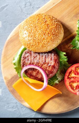 Primo piano sugli ingredienti del hamburger. Hamburger fatti in casa con carne di manzo, formaggio, cipolla, pomodoro e lattuga su un asse di legno, top shot Foto Stock