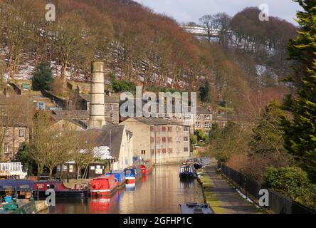 Colline ricoperte di alberi con una spolverata di neve, vecchi mulini e lunghe barche colorate sul canale Rochdale in Hebden Bridge, West Yorkshire, Inghilterra Foto Stock