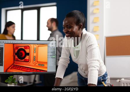 Designer multietnico che guarda computer con doppio display che lavorano insieme al progetto di gioco in ufficio aziendale. Lavoratori dei videogamer che sviluppano nuove applicazioni di gioco su pc con tecnologia moderna Foto Stock