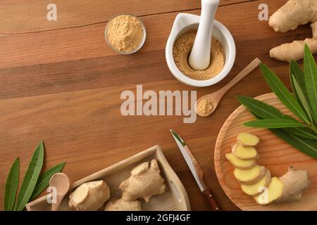 Preparazione allo zenzero in polvere per scopi curativi e culinari con radice di zenzero tagliata a porzioni su tavola di legno. Vista dall'alto. Foto Stock