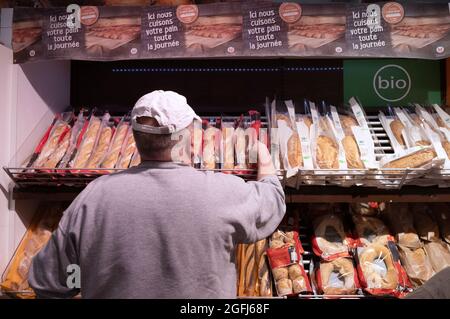 Supermercato Super U: L'uomo visto da dietro nel reparto del pane, pane biologico Foto Stock