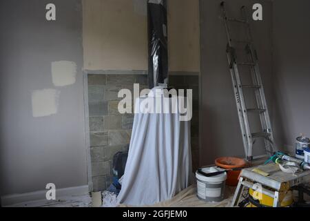 Camera in fase di ridecorazione, pareti preparate per la pittura, e stufa coperta per la protezione Foto Stock