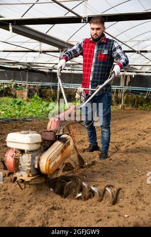 Giardiniere che utilizza un coltivatore motorizzato in serra Foto Stock