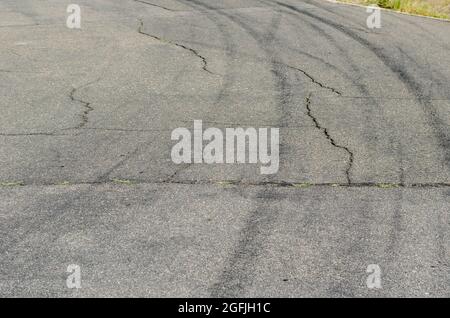 Asfalto grigio con cingoli pneumatici neri. Una vecchia strada di campagna con crepe. Cingoli delle ruote curvi in curva in autostrada. Foto Stock