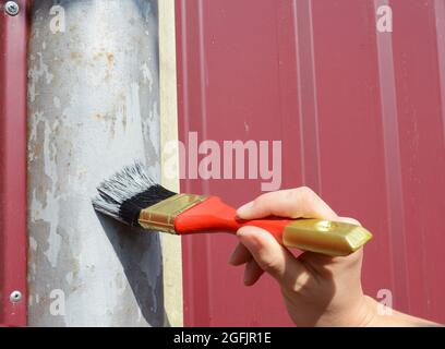 Un artigiano sta verniciando il palo di recinzione di metallo con una spazzola che applica il nastro di mascheratura, nastro del pittore per non versare la vernice sulla recinzione. Foto Stock