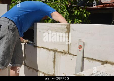 Un appaltatore di edifici sta costruendo una parete di casa da grandi blocchi di calcestruzzo cellulare autoclavati utilizzando la livella a bolla d'aria. Foto Stock