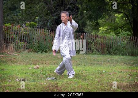 Un uomo di mezza età in esercizi tradizionali di abbigliamento Tai Chi in un parco a Queens, New York City. Foto Stock