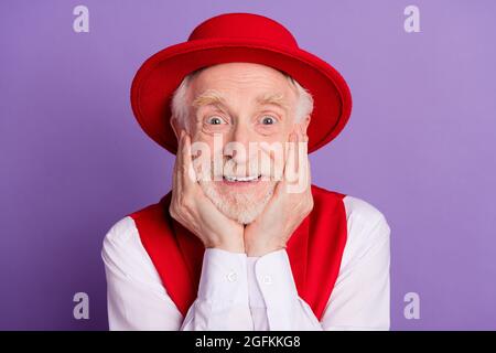 Foto di felice positivo stupito vecchio uomo tenere le mani guance buon umore sorriso isolato su sfondo di colore viola Foto Stock