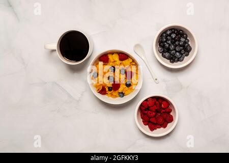 La colazione del mattino comprende cereali al fiocco di mais con lamponi freschi e mirtilli con caffè nero Foto Stock