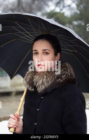 Ritratto di bella ragazza giovane tiene ombrello nel parco invernale Foto Stock