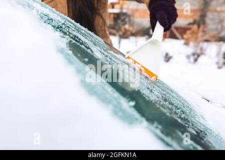 La donna pulisce la neve dalla sua auto con un raschietto Foto Stock