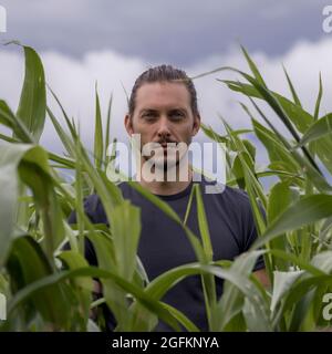 Giovane uomo in piedi in campo di mais, ritratto, fuoco morbido Foto Stock