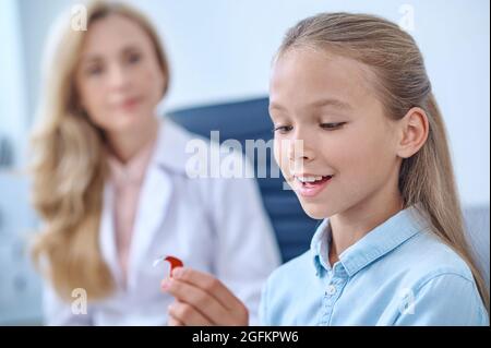 Ragazza felice età della scuola che ammira gli apparecchi acustici Foto Stock